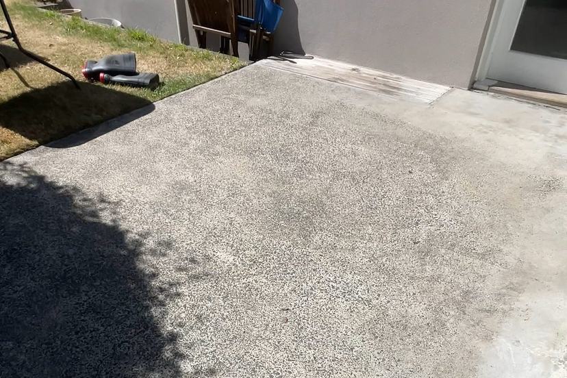 Clean concrete patio slab beside a house after pressure cleaning