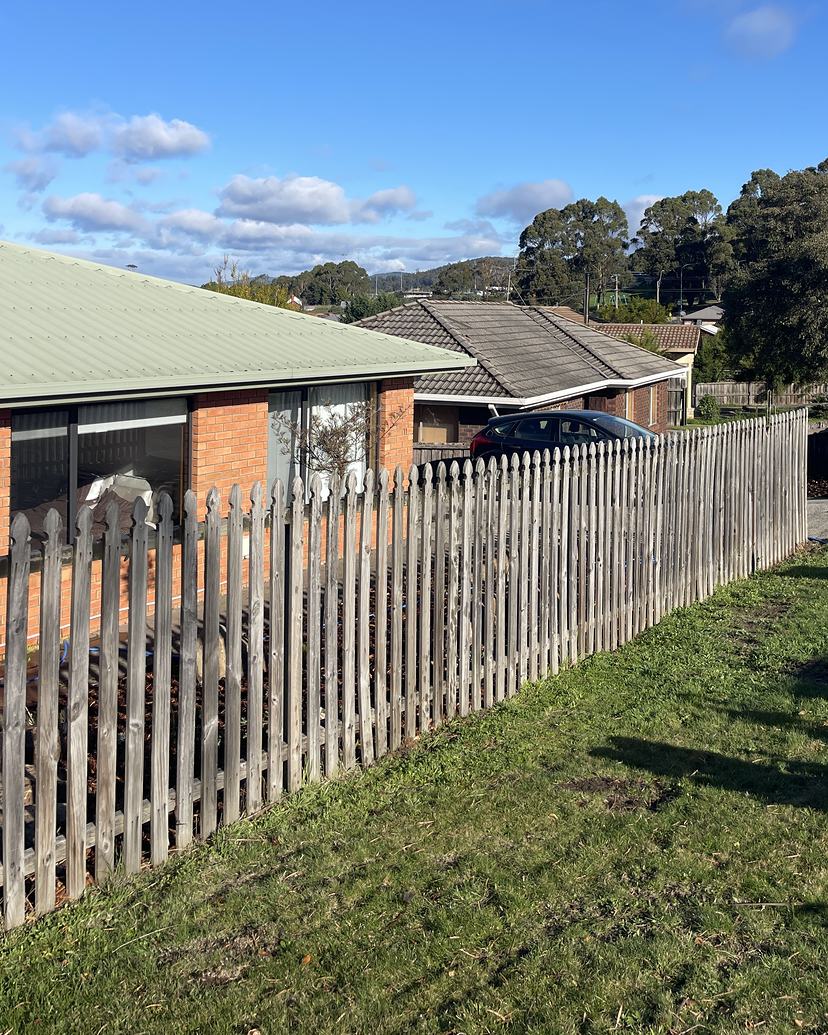 Weathered grey timber picket fence along a front lawn, before cleaning