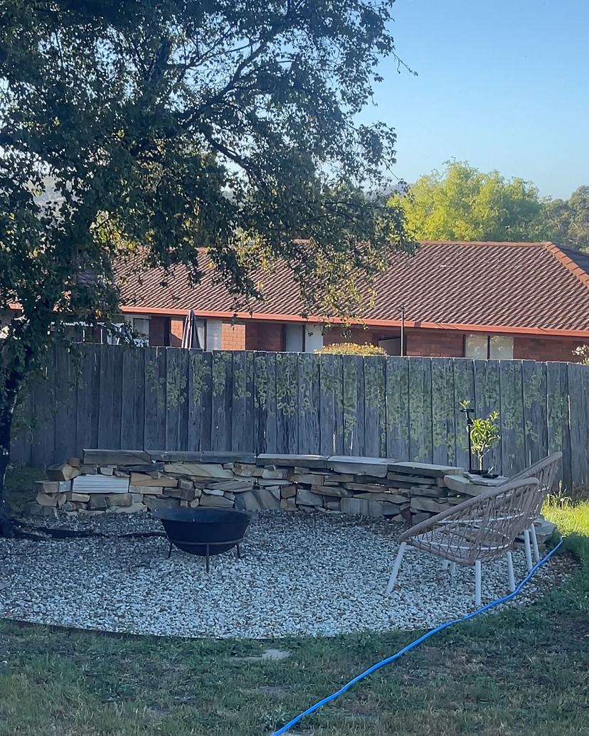 Rough-sawn timber fence grey and covered in lichen behind a sandstone seat wall and fire pit, before cleaning