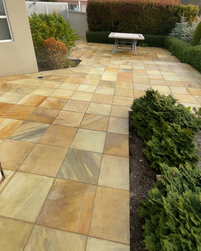 Golden sandstone courtyard in Sandy Bay after cleaning, bush-covered hills behind