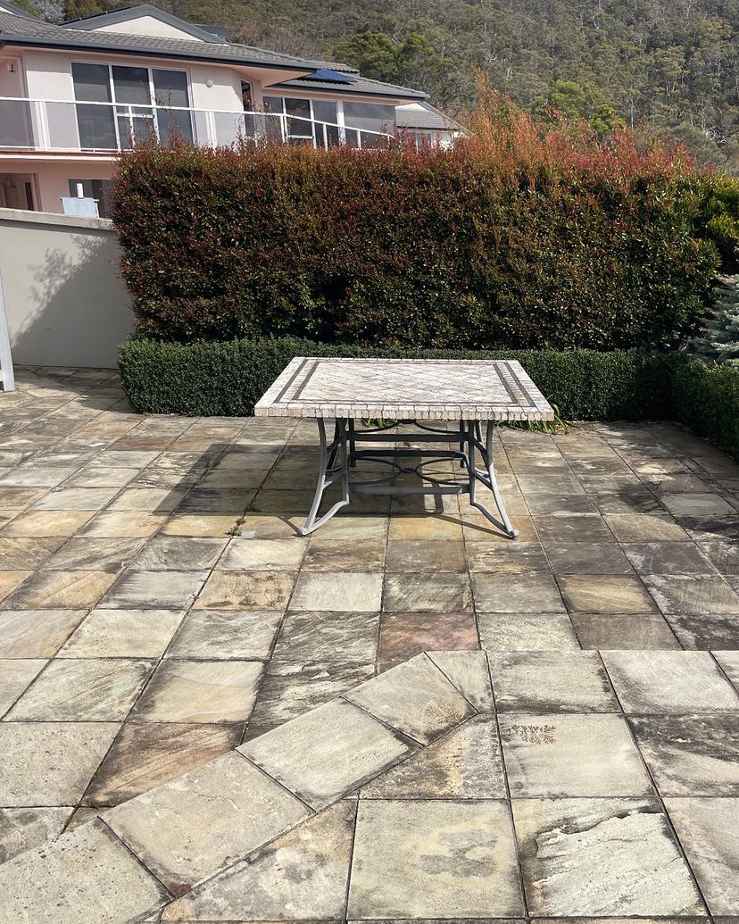 Sandstone courtyard in Sandy Bay stained dark grey with mould and grime, before cleaning